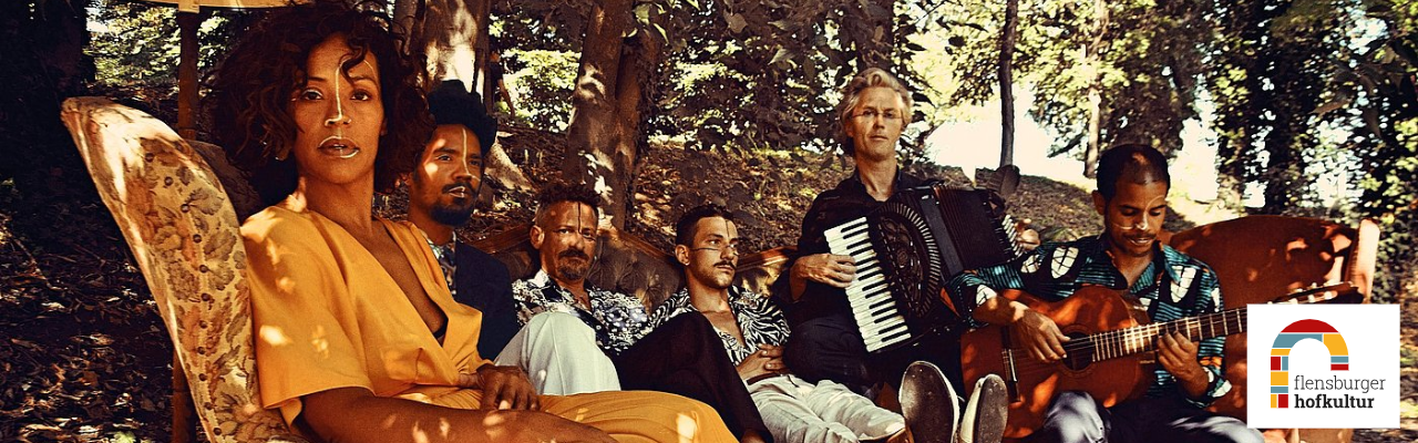 Eine sechsköpfige Band sitzt auf Sofas in einer herbstlichen Waldkulisse; unten rechts das Logo der Flensburger Hofkultur.