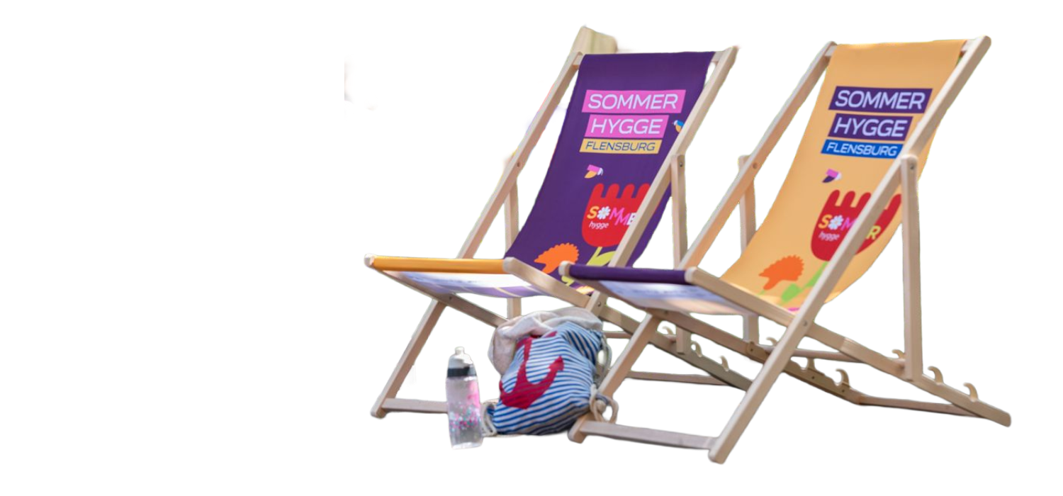 Zwei bunte Holzliegestühle mit dem Aufdruck Somme Hygge. Vor den Stühlen steht eine Trinkfalsche und ein Sportbeutel mit einem Anker drauf.